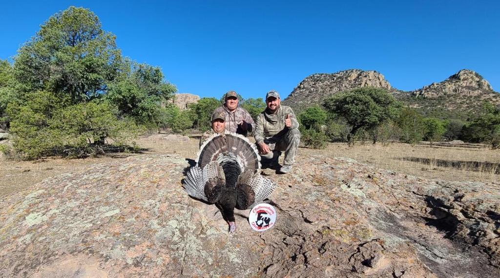 Three hunters with a Gould's turkey, rock outcrop behind